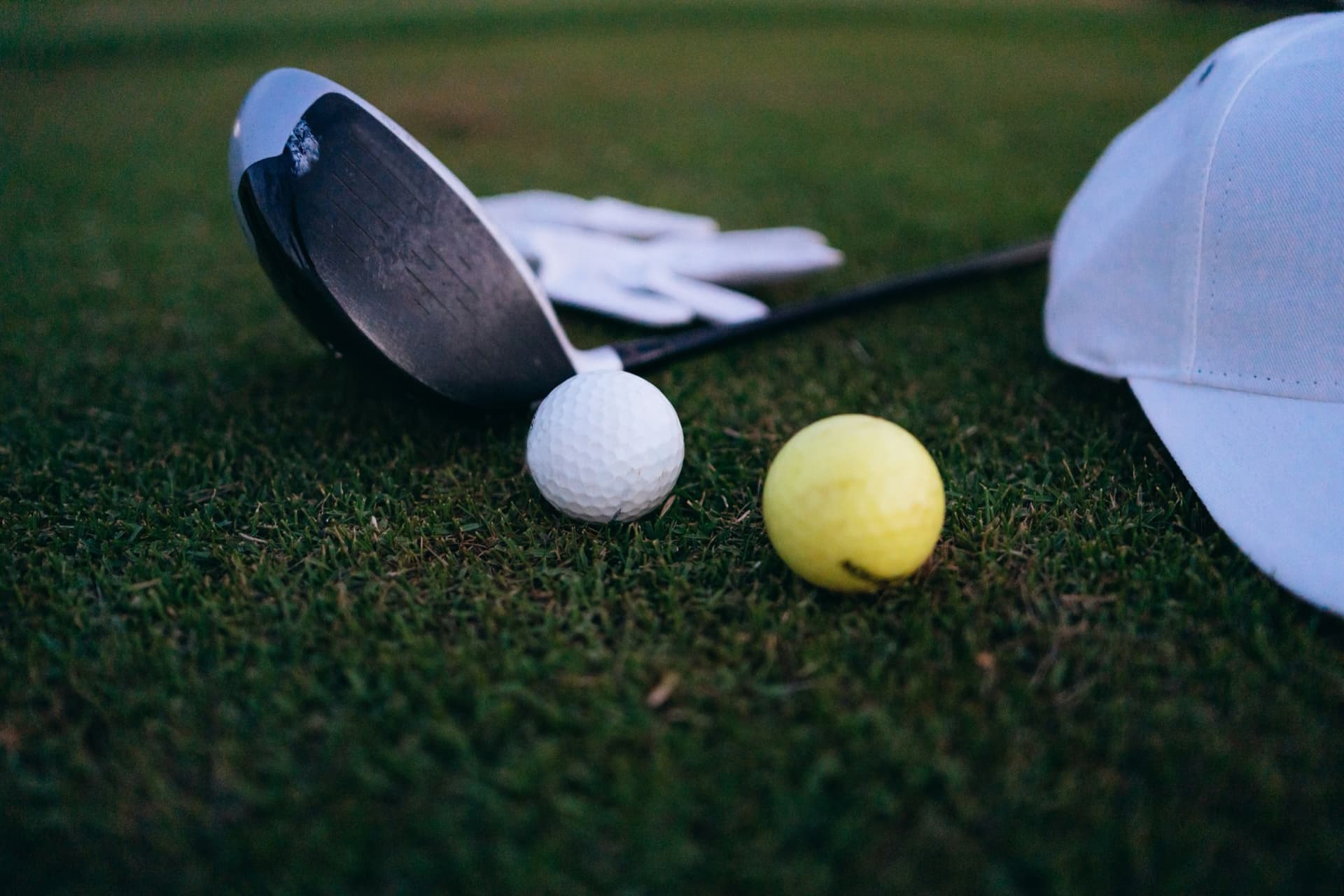 A driver, golf balls and a cap resting on the grass at dusk