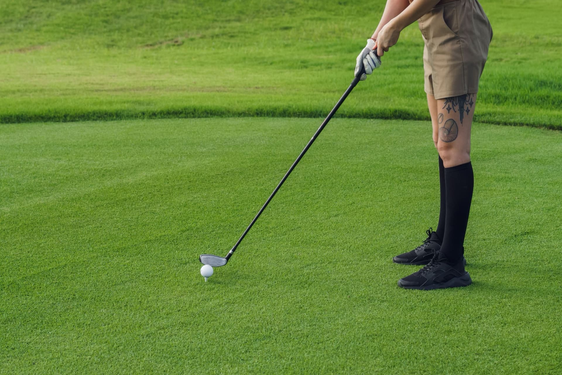A golfer in sneakers and knee socks addressing a teed-up ball